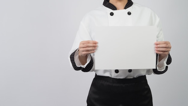 Donna che indossa l'uniforme da chef e tiene in mano un foglio A4 su sfondo bianco.