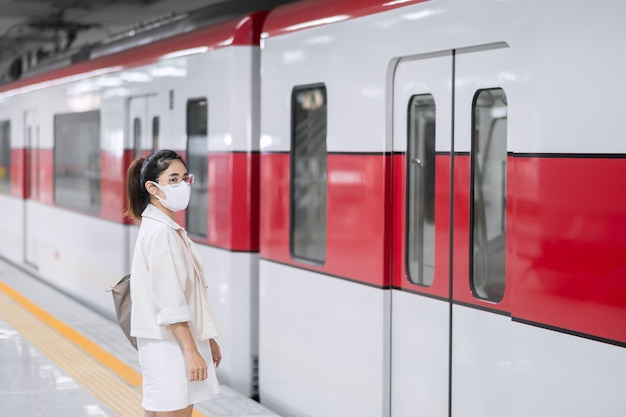 Donna che indossa la maschera protettiva per prevenire l'inflessione del coronavirus durante l'attesa del treno. trasporto pubblico. distanziamento sociale, nuova normalità e sicurezza durante la pandemia di covid-19