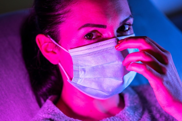 Donna che indossa la protezione della maschera facciale del virus in luci uv al neon luminose colorate in posa in un club o discoteca