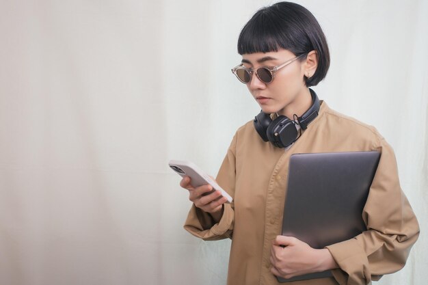 Donna che indossa le cuffie utilizzando il telefono e tenendo il computer portatile