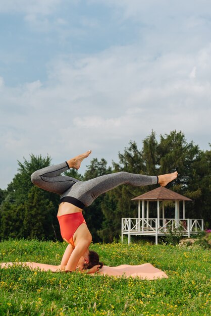 Donna che indossa leggings comodi a praticare yoga sulla testa di formazione all'aperto