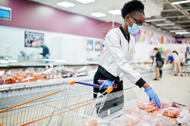 donna che indossa maschera medica monouso e guanti shopping nel supermercato durante l'epidemia di pandemia di coronavirus.