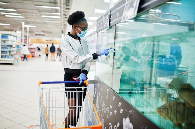 donna che indossa maschera medica monouso e guanti shopping nel supermercato durante l'epidemia di pandemia di coronavirus.