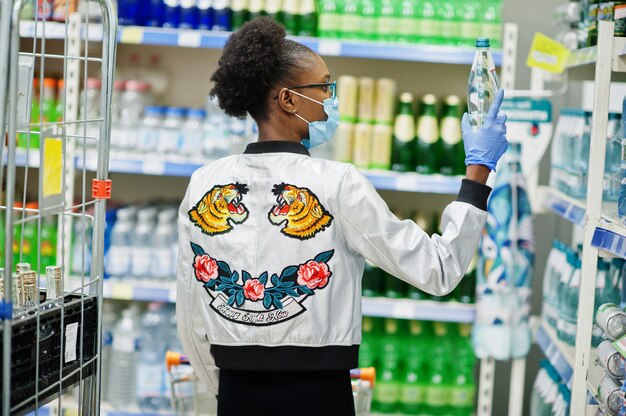 donna che indossa maschera medica monouso e guanti shopping nel supermercato durante l'epidemia di pandemia di coronavirus.