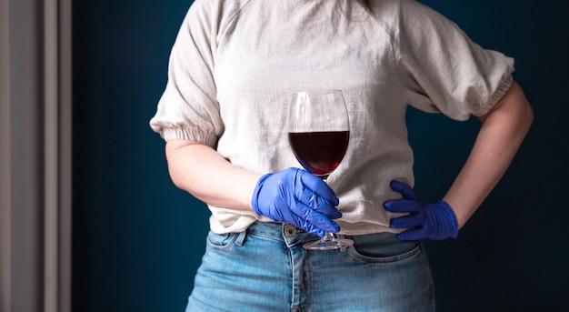 Donna che indossa maschera protettiva e guanti blu nella sua casa e bere vino rosso, auto isolato per Coronavirus Covid-19