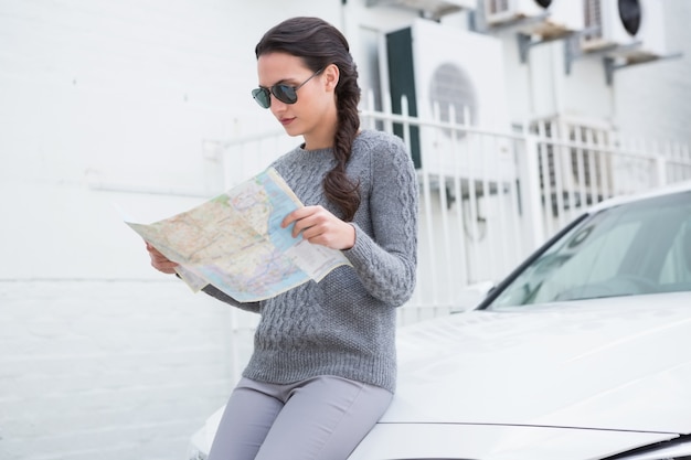 Donna che indossa occhiali da sole leggendo la mappa accanto alla sua auto