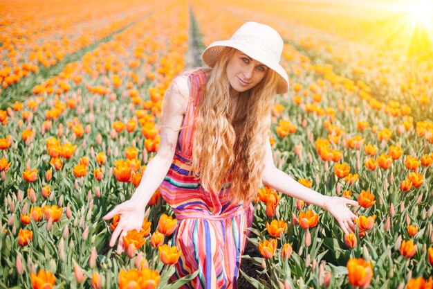 Donna che indossa un cappello e un vestito colorato in un campo di tulipani arancioni con luce solare intensa