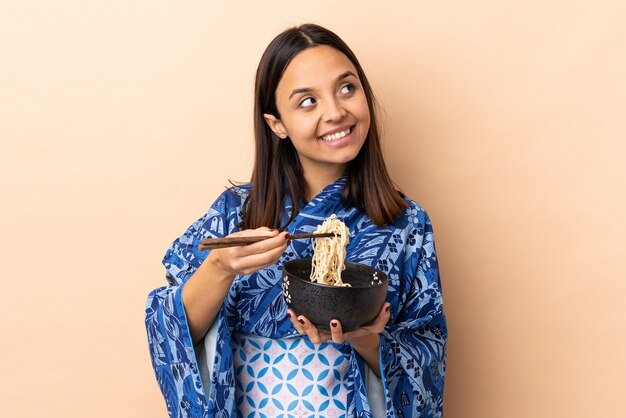 Donna che indossa un kimono e che tiene una ciotola piena di noodles tenendo una ciotola di noodles con le bacchette e guardando in alto