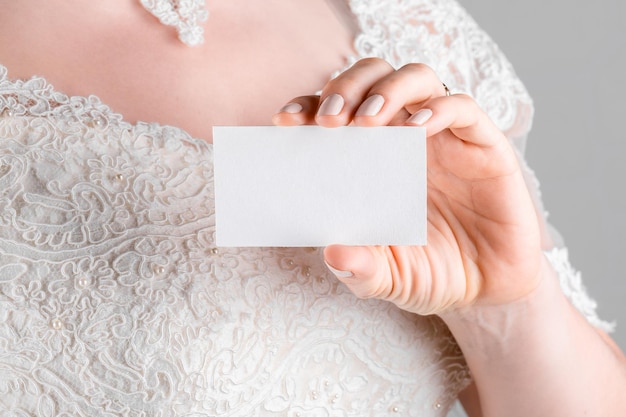 Donna che indossa un vestito da sposa che tiene in mano un cartellino di stagioneria da sposa modello x sullo sfondo bianco della parete