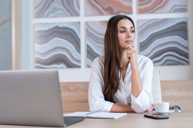 Donna che indossa una camicia bianca seduta Tavolo con laptop e notebook per prendere appunti Concetto di lavoro