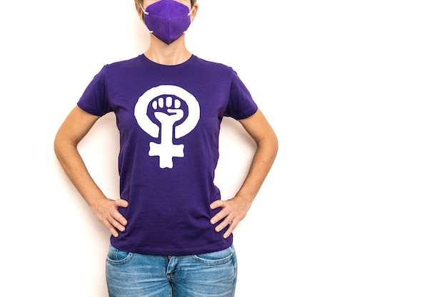 Donna che indossa una maglietta viola con il simbolo della donna lavoratrice che rivendica i diritti delle donne per la Giornata internazionale della donna l'8 marzo e indossa una maschera per la pandemia di coronavirus del 2020