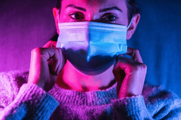 Donna che indossa una maschera facciale anti virus con luci uv al neon colorate e luminose in posa a casa