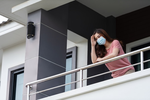 Donna che indossa una maschera facciale e mette in quarantena nel balcone della sua casa, concetto di pandemia di coronavirus (covid-19)