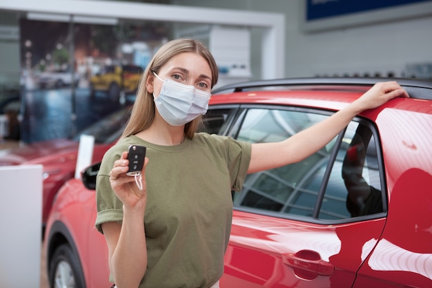 Donna che indossa una maschera medica mentre acquista una nuova auto presso un concessionario di auto, mostrando la chiave dell'auto