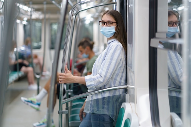 Donna che indossa una maschera medica nell'auto della metropolitana ragazza in maschera chirurgica sicura nel trasporto pubblico