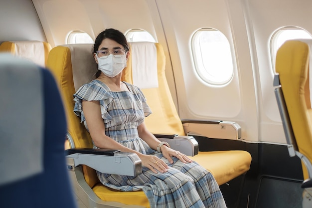Donna che indossa una maschera protettiva seduta in aereo o con i mezzi pubblici, protezione Infezione da malattia di Coronavirus, turista pronto a viaggiare. Successivo Normale, turismo e concetto di riapertura