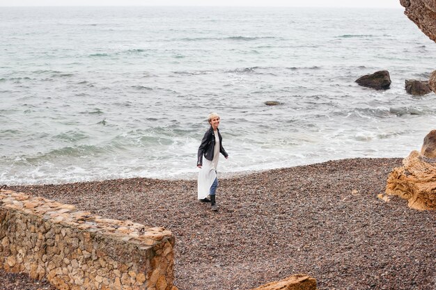 Donna che indossa vestito e giacca che cammina vicino al mare in autunno