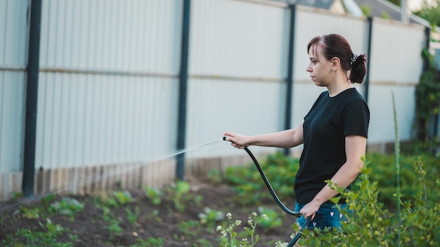 Donna che innaffia il giardino con un tubo Donna che spruzza acqua sulle verdure con un tubo da giardino Una donna felice con un tubo si prende cura del giardino Concetto di giardinaggio e cura del giardino