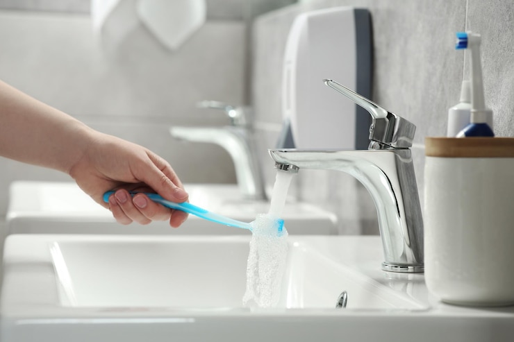 Foto donna che lava spazzolino da denti in plastica sotto l'acqua corrente dal rubinetto in primo piano del bagno