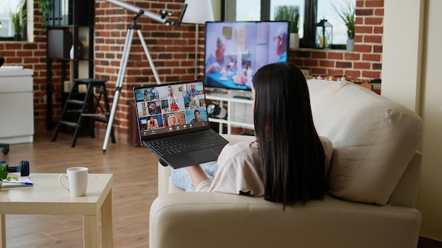 Donna che lavora a distanza da casa durante la videochiamata della riunione online sul laptop seduto sul divano dell'appartamento. Libero professionista che lavora da casa mentre discute con i colleghi in una conferenza su Internet.