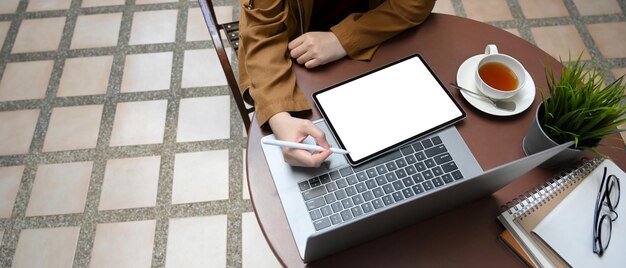 Donna che lavora a distanza in un bar all'aperto utilizzando laptop e tablet tablet mockup schermo bianco