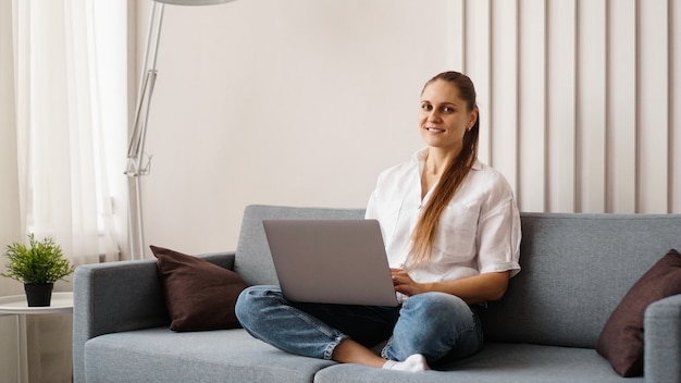 Donna che lavora al computer portatile da casa o studente che studia da casa o libero professionista. Donna moderna di affari in una camicia bianca e jeans.