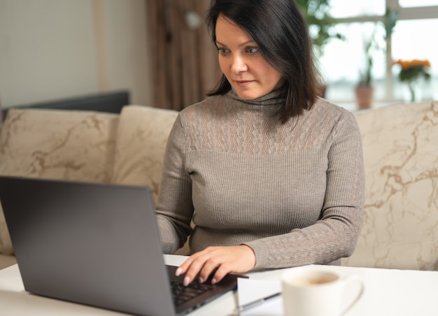 Donna che lavora al computer portatile in remoto sullo sfondo dell'interno del soggiorno Lavoro a distanza