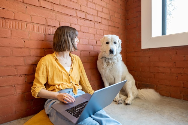 Donna che lavora al computer portatile mentre è seduta con il suo cane a casa