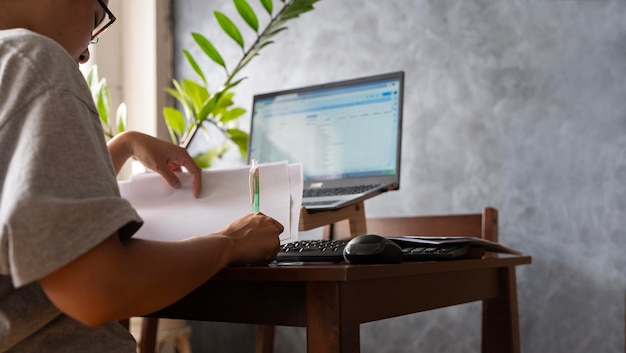 Donna che lavora al portatile in ufficio a casa mentre guarda i documenti in un'atmosfera di luce calda attraverso la finestra Donna stressata che lavora da casa al portatile in cucina