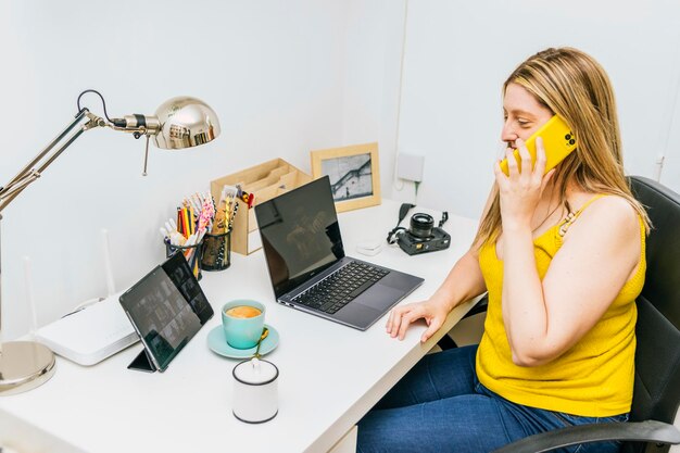 Donna che lavora in ufficio da casa utilizzando il telefono e il laptop Lavora da casa Concetto di telelavoro