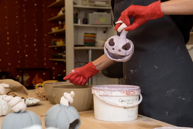 Donna che lavora in un laboratorio di ceramica che produce portacandele in ceramica a forma di zucca per Halloween cel