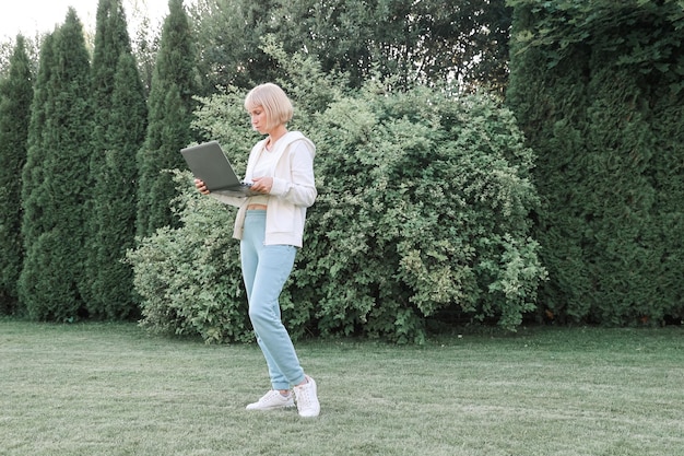 Donna che lavora nel parco con telefono e laptop Imprenditrice lavora all'aperto verde natura sfondo Connessione di rete Wi-Fi accesso gratuito Libero professionista che si rilassa nella natura e utilizza la tecnologia