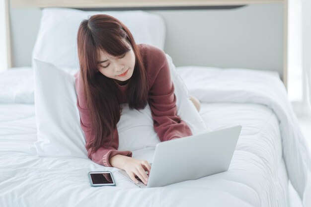 Donna che lavora su un computer portatile seduto sul letto in casa.