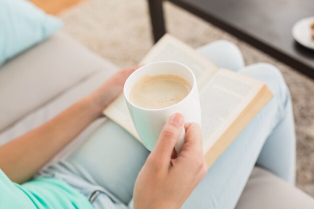 Donna che legge e che beve caffè sul divano