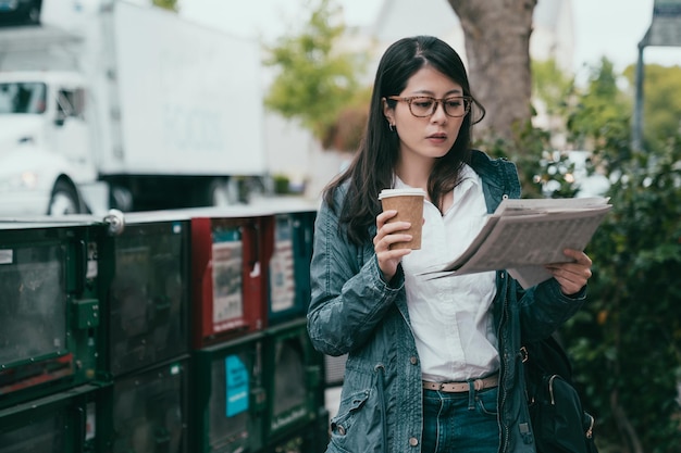 donna che legge il giornale e sembra seria in faccia con una tazza di caffè in mano.