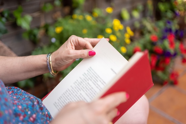 Donna che legge un libro in giardino con piante con fiori di diversi colori