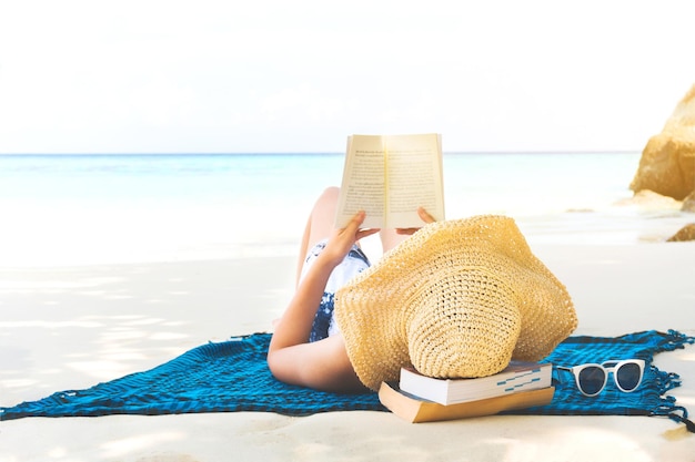 Donna che legge un libro mentre giace sulla spiaggia contro il cielo