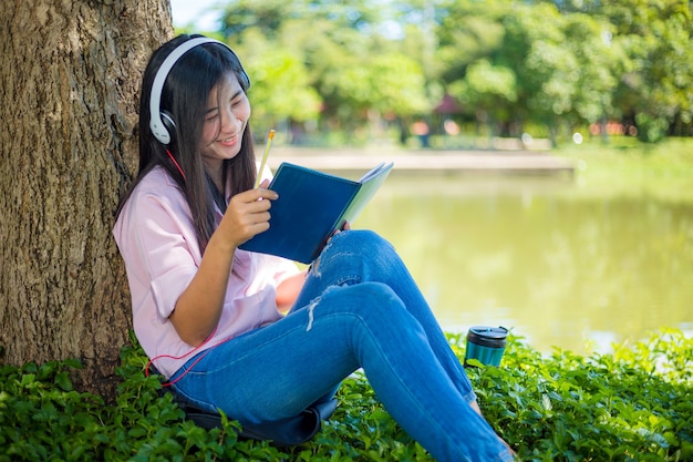 donna che legge un libro nel parcoBella giovane donna seduta in foglie d'autunno sotto l'albero