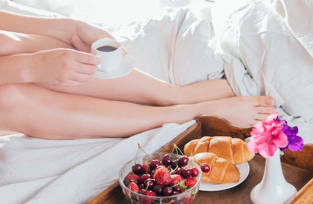 Donna che mangia caffè e croissant con frutti di bosco a letto