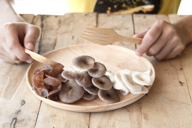donna che mangia il fungo commestibile differente in piatto di legno con il cucchiaio e la forchetta sulla tavola di legno