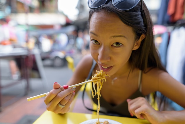 Donna che mangia le tagliatelle tailandesi del pad alla strada di Khao San