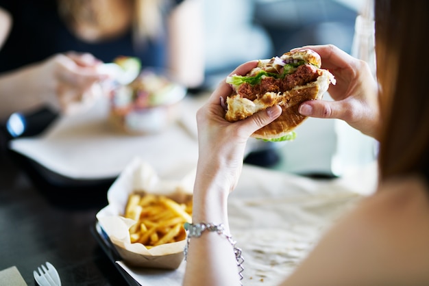 Donna che mangia mangiare hamburger senza carne vegano nel ristorante