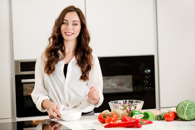 Donna che mangia minestra in cucina dove cucina verdure