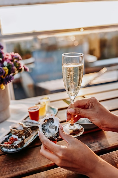 Donna che mangia ostriche fresche e beve vino prosecco freddo al tramonto estivo Prelibatezze di mare