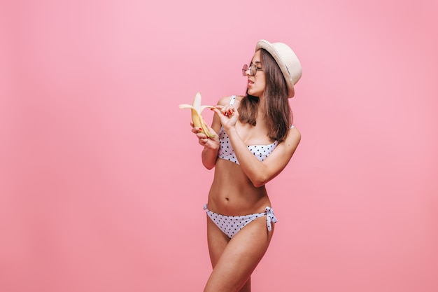 donna che mangia una banana su una parete rosa
