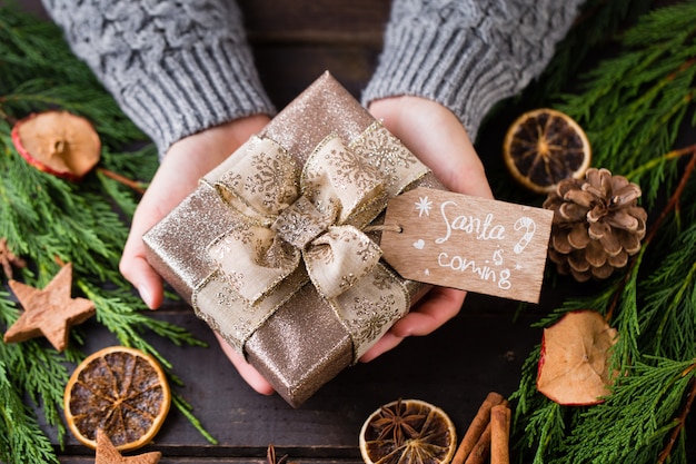 Donna che mantiene i regali di Natale posati su uno sfondo di tavolo in legno.