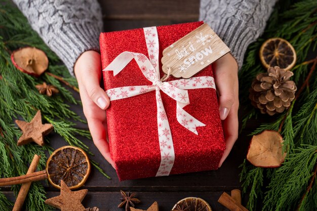 Donna che mantiene i regali di Natale posati su uno sfondo di tavolo in legno.