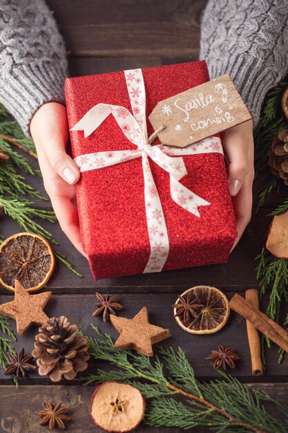 Donna che mantiene i regali di Natale posati su uno sfondo di tavolo in legno.