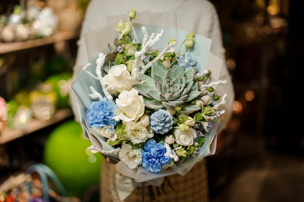 Donna che mantiene un bouquet di rose bianche, garofani, rami artificiali e piante grasse