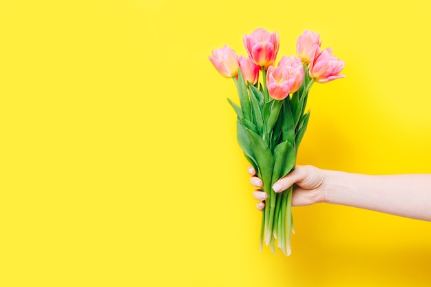 Donna che mantiene un bouquet primaverile di tulipani rosa in mano su giallo